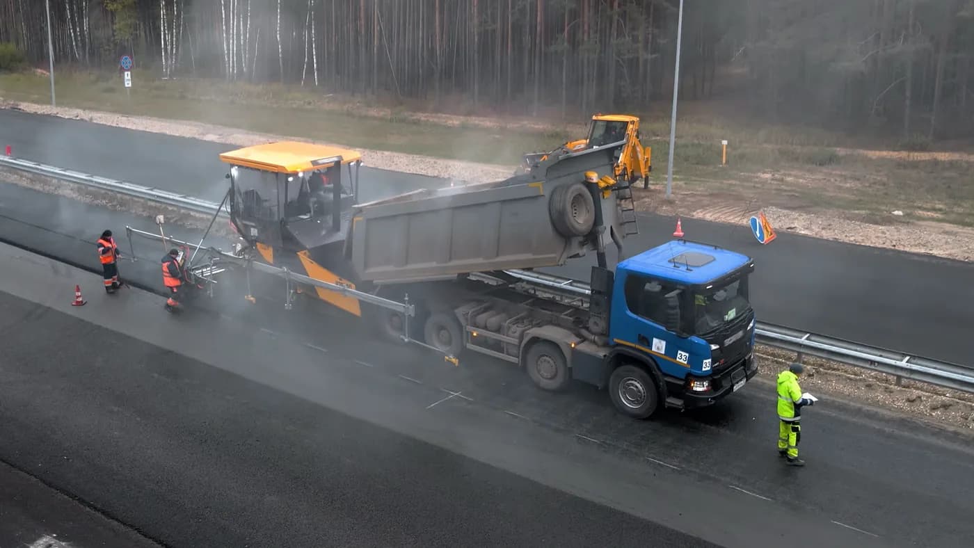 Asphalt paver working behind a dump truck with ground crew alongside the mat