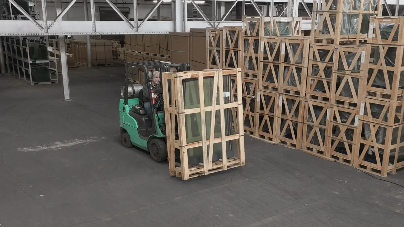 Forklift moving a crated glass panel through a warehouse aisle