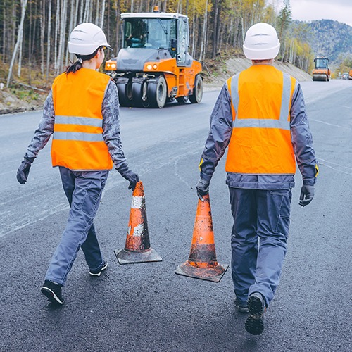 two construction worker, each carrying a traffic cone